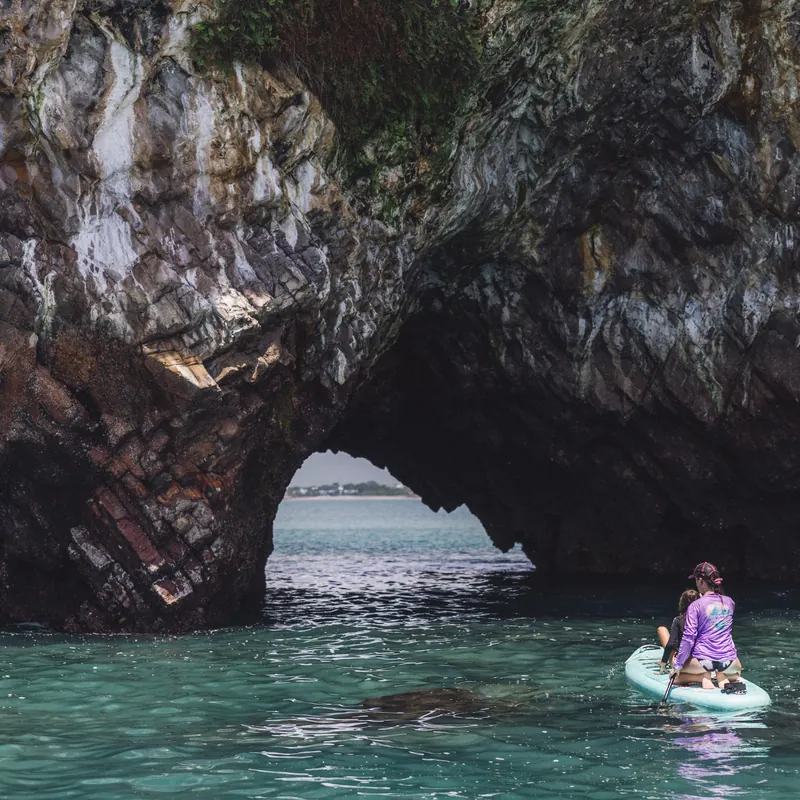 Paddleboarder exploring a sea arch at Isla Farallón